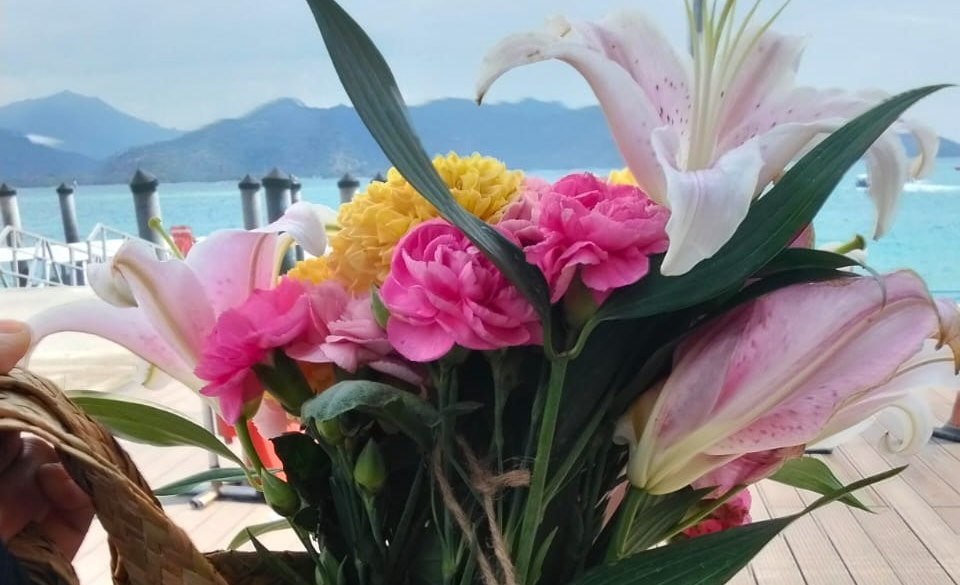 Colorful Island Bloom bouquet in a woven basket by the sea
